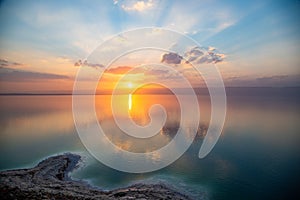 Sunset over Dead sea, view from Jordan to Israel and Mountains of Judea. Reflection of sun, skies and clouds. Salty beach, salt.