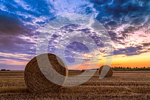 Sunset over farm field with hay bales