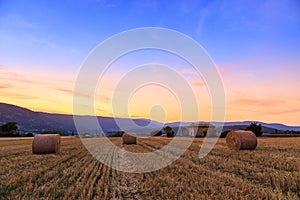 Sunset over farm field with hay bales near Sault