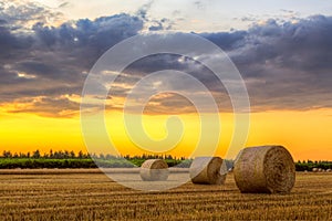 Sunset over farm field with hay bales