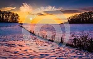 Sunset over a fence in a snow covered farm field in rural Carroll County, Maryland. photo