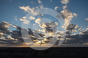 Sunset over the forest with sun rays breaking through clouds