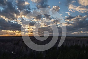 Sunset over the forest with sun rays breaking through clouds