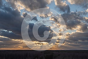 Sunset over the forest with sun rays breaking through clouds