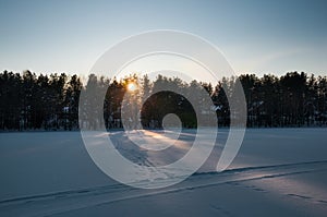 Sunset over the frozen lake and pine forest. Footsteps tracks on the snow