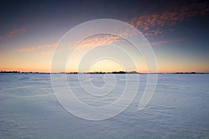 Sunset over a frozen snow covered field.