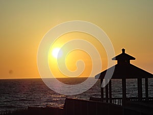 Sunset over gazebo on ocean waterfront.