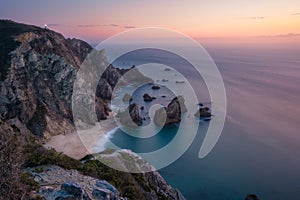 Sunset over a hidden surreal Praia Da Ursa Beach. Cabo Da Roca with light-house in background. Atlantic coast, Portugal