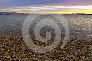 Sunset over hills and mountains with a calm ocean and rock and sand beach in the foreground