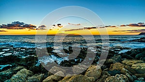 Sunset over the horizon with a few clouds and the rocky shores of the west coast of Oahu