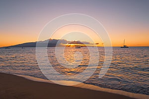 Sunset over island, sailboats, and sandy beach in Maui