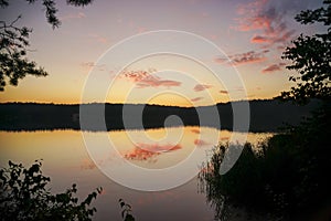 Sunset over the lake around which conifers grow. The sky is yellow and pink