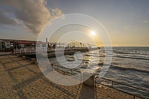 Sunset over the Mediterannean sea. Beautiful landscape of sandy beach with sea waves and wooden pier during sunset. Sky