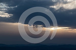 Sunset over mountains and valley, with sun hiding behind clouds