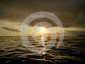 Sunset over the ocean with light reflecting on ocean waves moving with boats on the water in the distance