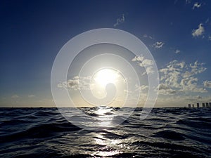 Sunset over the ocean with light reflecting on ocean waves moving with boats on the water in the distance