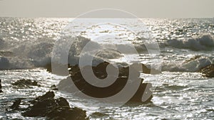 Sunset over ocean with rocks as waves crash in golden light. Natural seaside scene for relaxation, travel, nature docs