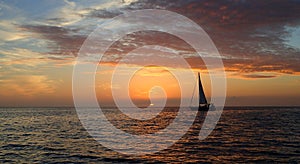 Sunset over the ocean with a sailboat sailing near the sun