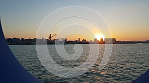 Sunset over the ocean and seaport. View of the sunset and the ocean through the porthole of the ship.View of the ocean and the cit