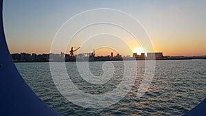 Sunset over the ocean and seaport. View of the sunset and the ocean through the porthole of the ship.View of the ocean and the cit
