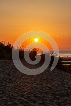 Sunset over the ocean with silhouetted marram grass on a sand dune in the foreground, at Formby in Merseyside