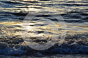 Sunset over the Ocean - View of the red sun sinking into the horizon and waves washing over the sand of the beach