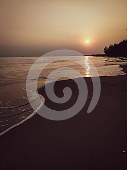 Sunset over the ocean with waves crashing on the shore