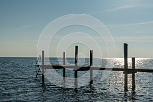 Sunset over the ocean with a wooden dock and ladder for swimming in the foreground