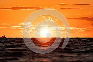 Sunset over the ocean with yellow and orange sun and orange glow reflecting in the water