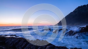 Sunset over the Pacific ocean. Long exposure photo of waves crashing onto basalt rocks.