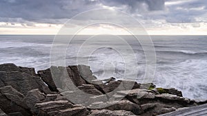 Sunset over rough ocean coast with waves and pancake like rocks in foreground, New Zealand