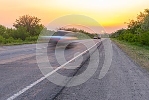 Sunset over rural road with speedy cars