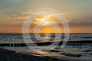 Sunset over the sea with breakwater, beach and birds