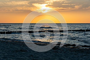 Sunset over the sea with breakwater, beach and birds