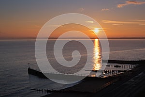 Sunset over the sea with a golden reflection of the sun reaching wooden groynes on a beach