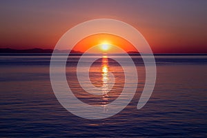 Sunset over sea horizon. Bright sun is reflected from water surface, evening sky