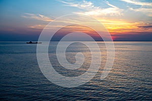 Sunset over the Sea of Japan. Blood red sun and colorful clouds on evening sky over the sea with cargo ship.