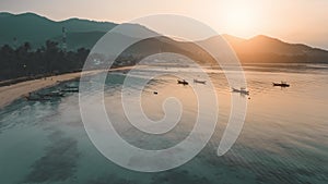 Sunset over sea and mountains. Boats on beach aerial view. Orange sun shines on calm ocean water.