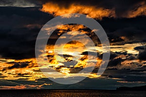 Sunset over stormy clouds across the water reflecting dark and looming dramatic sky moody