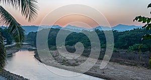 Sunset over the Thai-Burmese mountains with river and palm tree