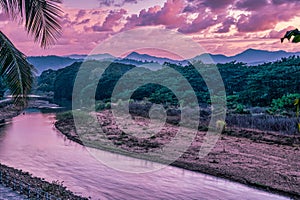 Sunset over the Thai-Burmese mountains with river and palm tree