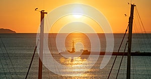 Sunset over Tinos island, Cyclades, Greece. View of beacon silhouette between ship mast, golden sun