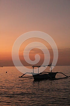 Sunset over the tranquil sea, with silhouette of boat on horizon. North Bali Indonesia.