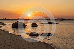 Sunset over a tropical beach with boulders in silhouette and orange reflections