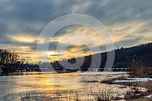 Sunset over the winter river. Thawing in the ice of a frozen river