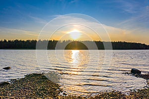 Sunset at the Paijanne lake. Beautiful scape with stone beach, pine forest and water. Lake Paijanne, Finland