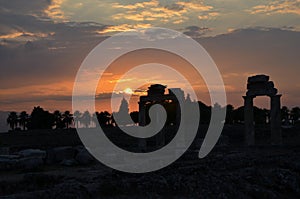 Sunset in Pamukkale, in the interior of Turkey, with the sun in the background and, in front, some trees and the ruins of an