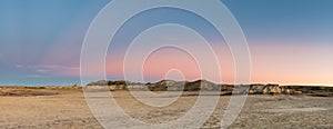 Sunset panorama of a flat, barren desert with colorful peaks and hills