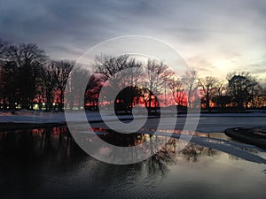 Sunset in a Park with Ice on Frozen Pond in Winter.