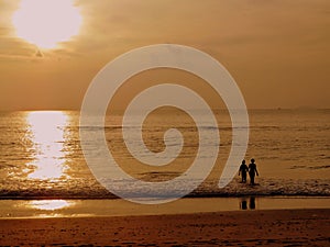 Sunset photo of a boy and girl walking into the sea while their reflection is cast on the beach behind them.